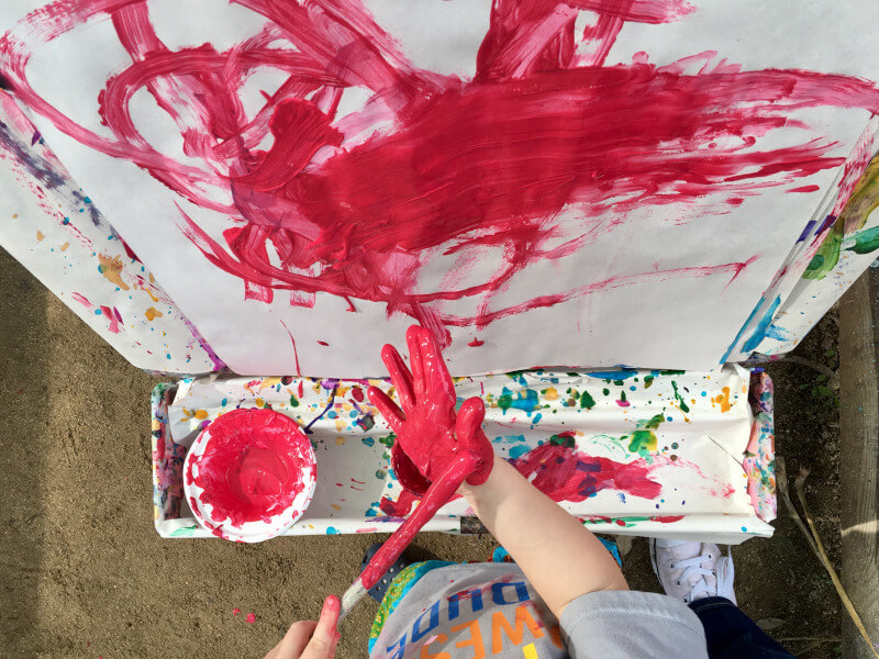Dziecko malujące obraz nakładając amarantową farbę na dłoń