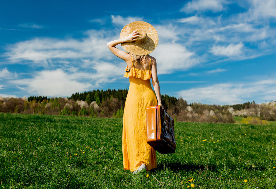 Kobieta na polanie ubrana w żółtą sukienkę maxi i słomiany kapelusz
