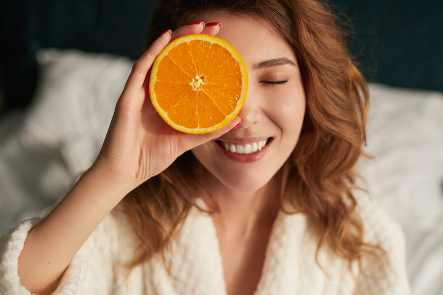 Kobieta w szlafroku zasłaniająca część twarzy połówką pomarańczy