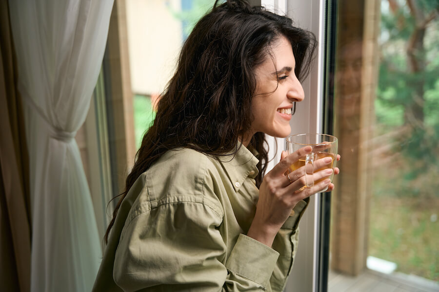 Uśmiechnięta brunetka z szklanką herbaty spoglądająca za okno