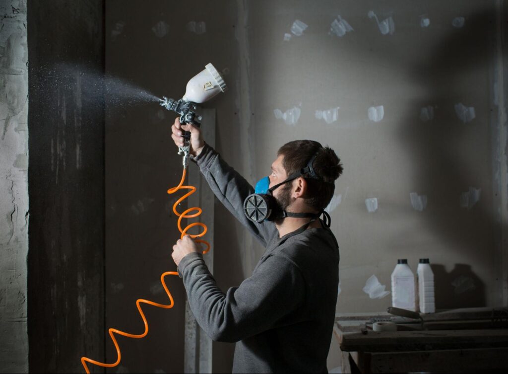 mężczyzna malujący ścianę pistoletem malarskim