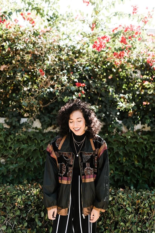 Uśmiechnięta kobieta, wzorzysta kurtka, spodnie w pasy, naszyjniki