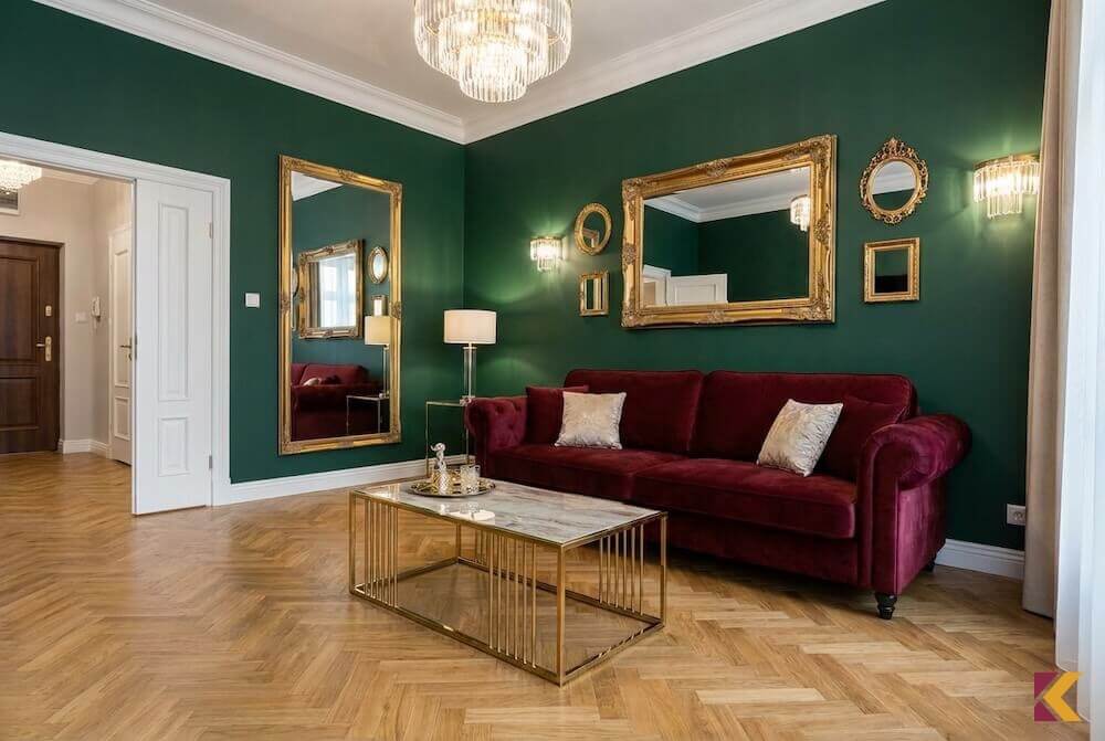Salon w stylu glamour z burgundową sofą na tle zielonej ściany