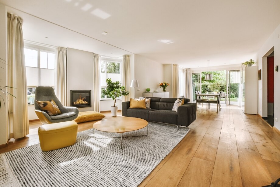 Stylowy salon, drewaniana podłoga, jasne ściany, kominek, szara sofa i fotel, miodowe dodatki